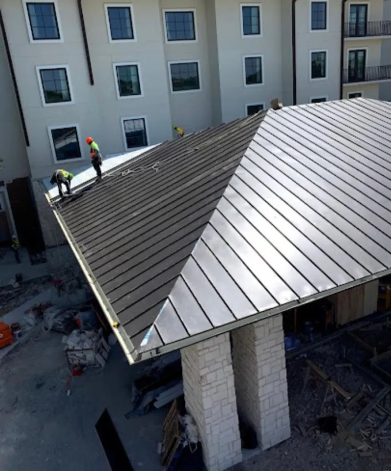 Crew installing standing seam metal roof panels on a commercial project in Lemay